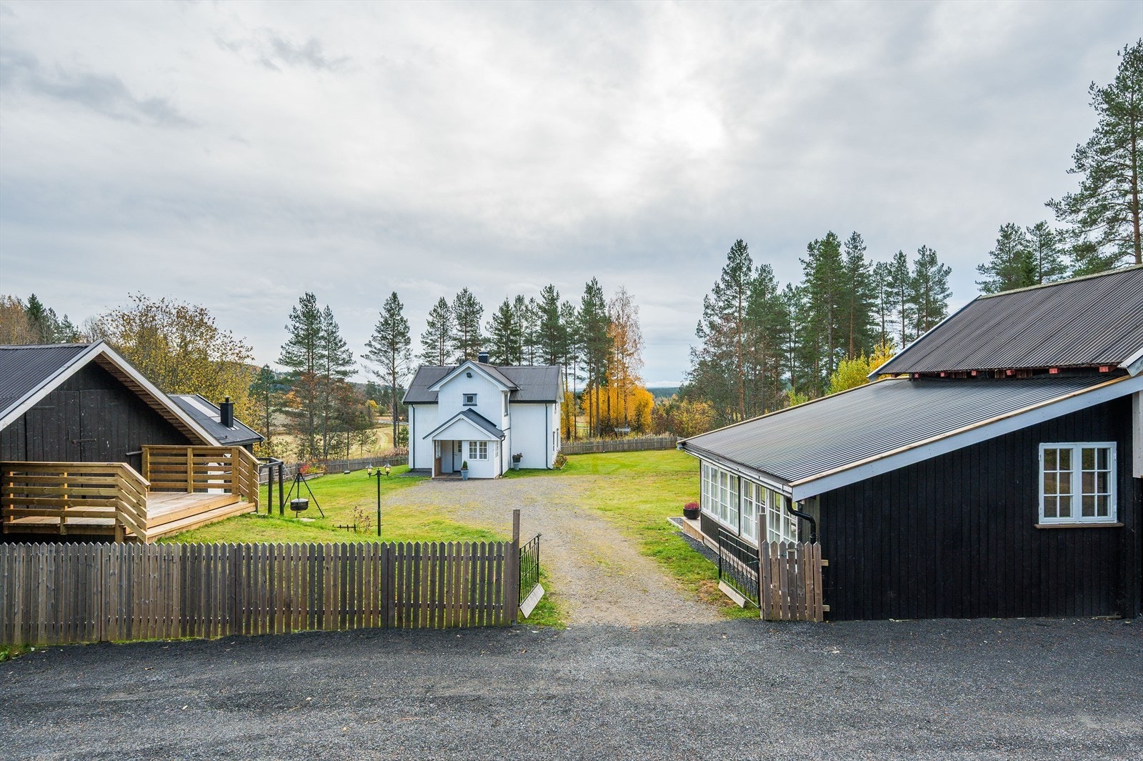 Gruset innkjøring med oppstillingsplass for flere kjøretøy. Gjerde rundt tunet som er pent opparbeidet med plen, rips, blåbær, stikkelsbær, rabarbra, urter og noe beplantning/blomster. Galleribilde
