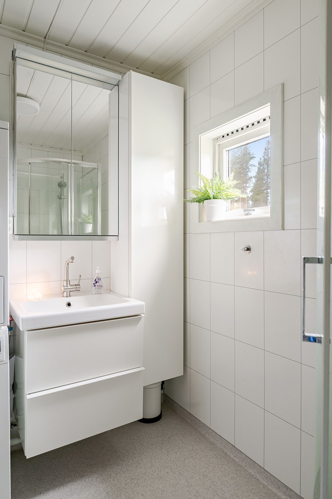 Moderne baderomsinnredning med skuffer og heldekkende servant, speilskap med belysning over, samt ekstra høyskap ved siden av. Badet er også utstyrt med dusjkabinett, toalett og opplegg for vaskemaskin/tørketrommel. Galleribilde