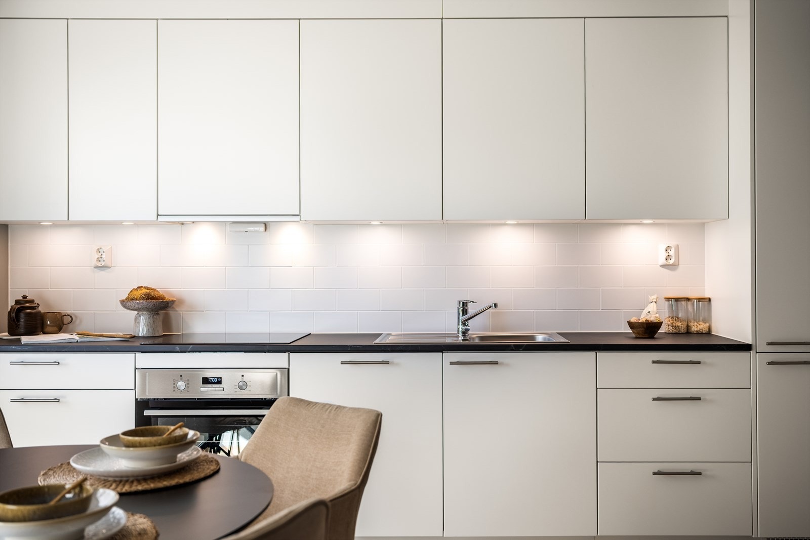 Kjøkkeninnredning med lyse, glatte fronter og en mørkere, slitesterk benkeplate i laminat. Galleribilde
