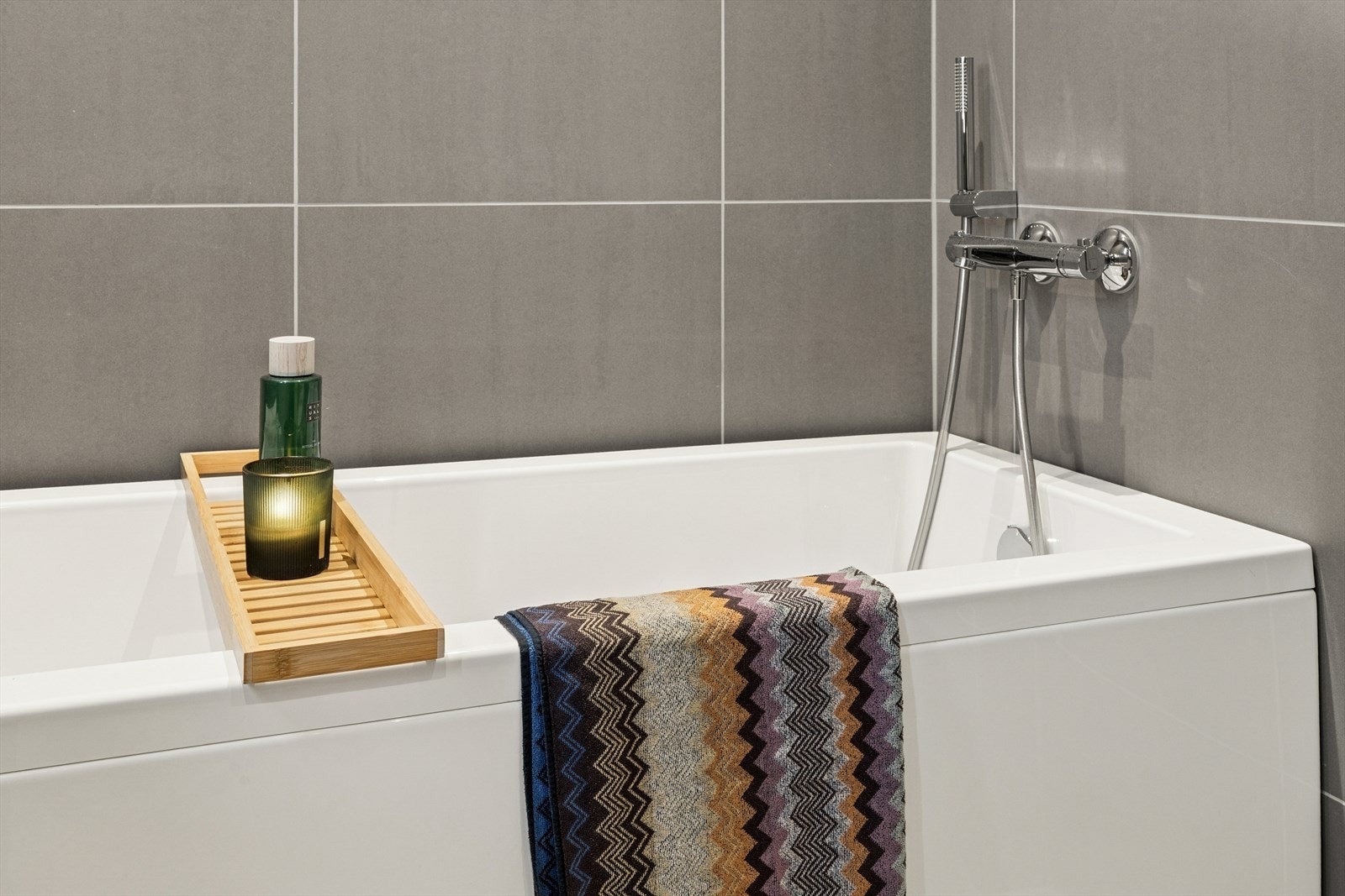 Baderommet er utstyrt med badekar, veggmontert toalett, servant m/skap i glatte fronter og dusjhørne med innfellbare dusjdører. Galleribilde