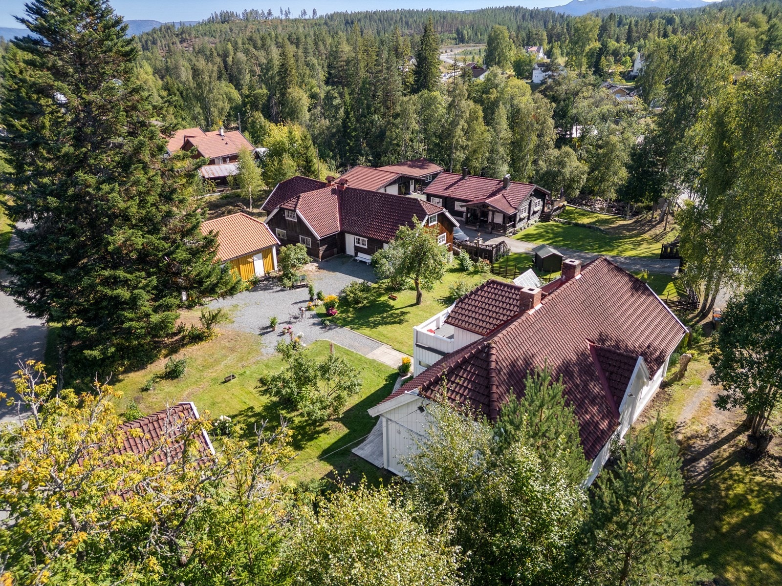 Dronebilde over tomta, med hovedhuset til høyre, låven i brunt, og bryggerhus og stabbur til venstre. Galleribilde