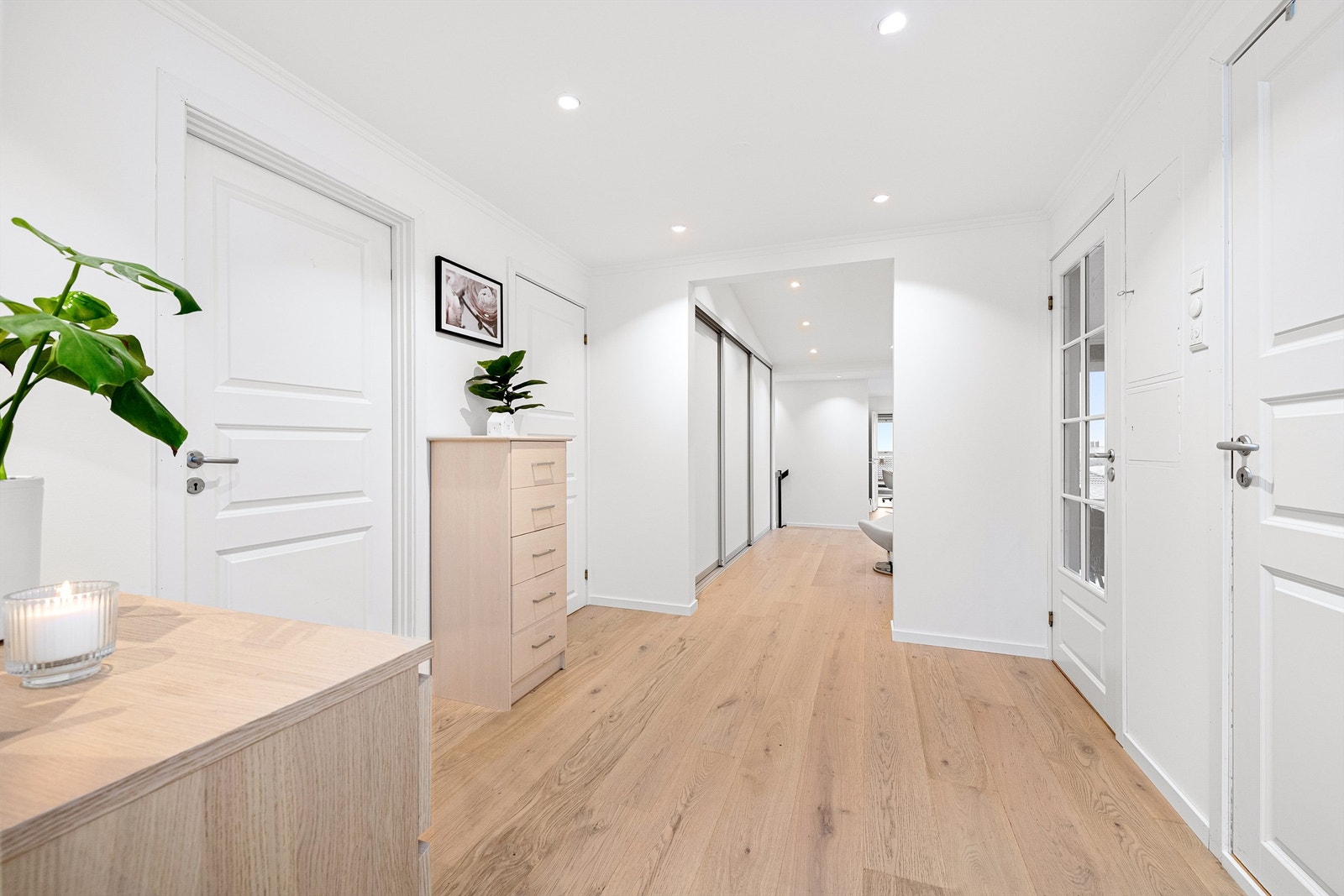 Stor og romslig gang/hall mot tilbygget del. Lyse overflater og hvite profilerte innerdører Galleribilde