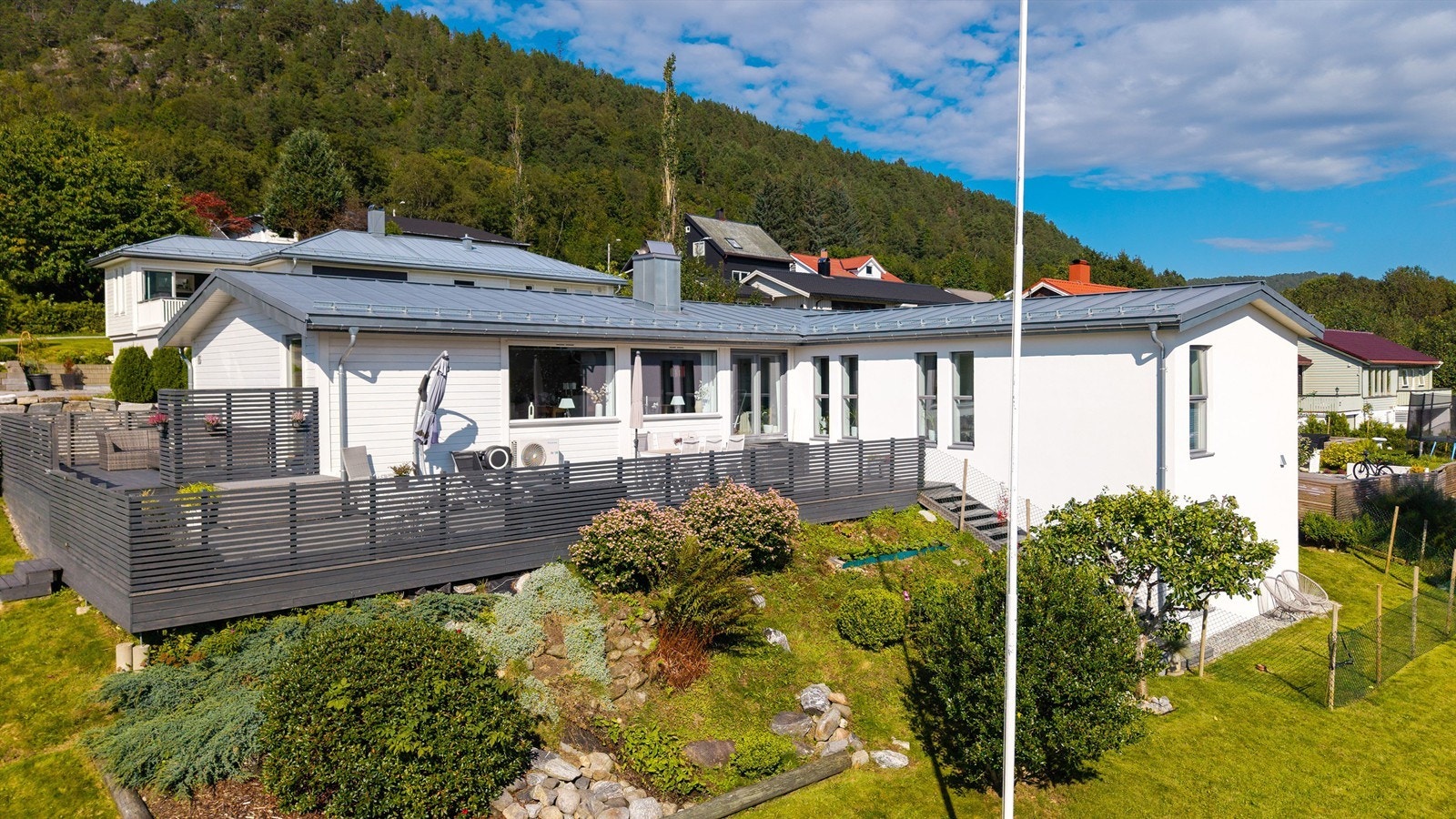 Dronebilde av fasade og terrasse med pent opparbeidet og beplantet hage Galleribilde