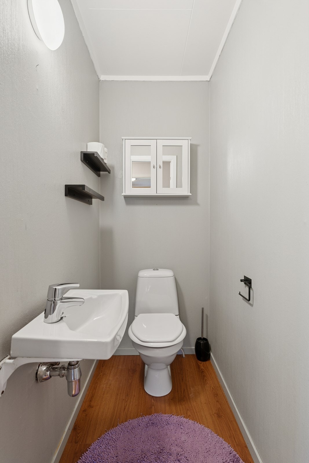 Toalettrommet har laminat på gulv, tapet på vegger og malte plater i tak. Rommet er innredet med vegghengt servant og gulvstående toalett. Galleribilde