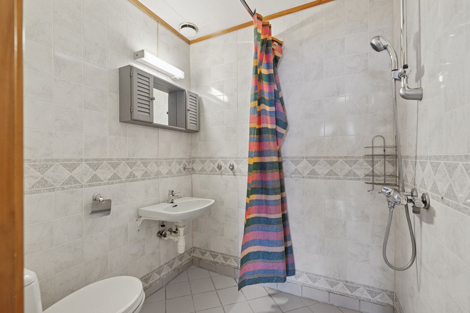 Badet er opplyst å være oppusset på midten av 90-tallet. Rommet er innredet med vegghengt servant, gulvstående toalett og dusj med forheng. Galleribilde