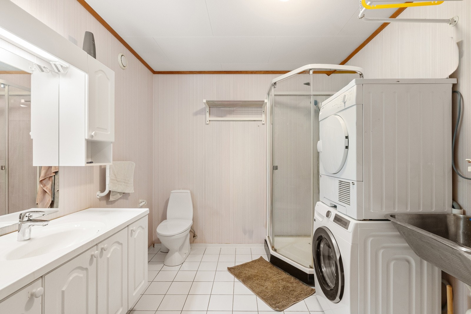Badet har fliser på gulv med varmekabler, toalett, seksjon med hel servant, dusjkabinett og opplegg for vaskemaskin. Galleribilde