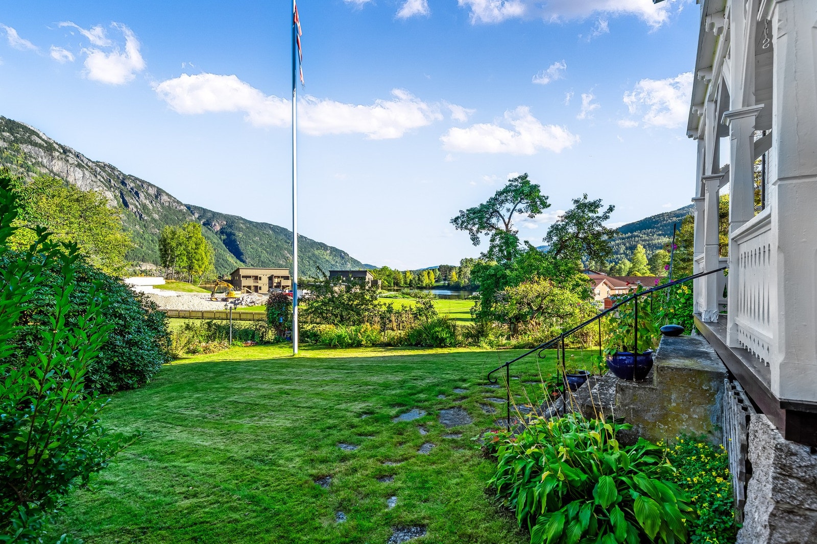 Vakker og opparbeidet hage med store grønne plener, gamle trær, frodig beplantning og rosebusker. Den grusede innkjørselen, tregjerdet og flaggstangen gir eiendommen en klassisk og harmonisk ramme. Galleribilde