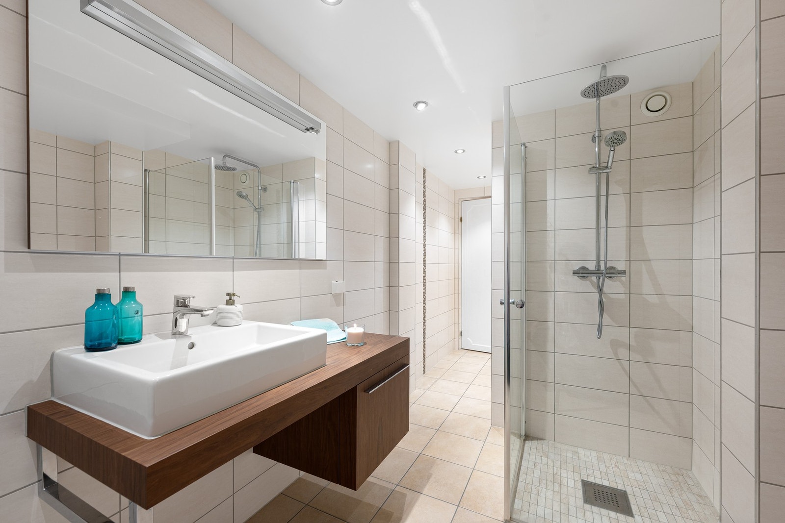 Badet er utstyrt med et praktisk servantskap, speil med integrert belysning og et dusjhjørne med stilrene, innfellbare glassdører. Her finner du både hånddusj og regndusj. Galleribilde