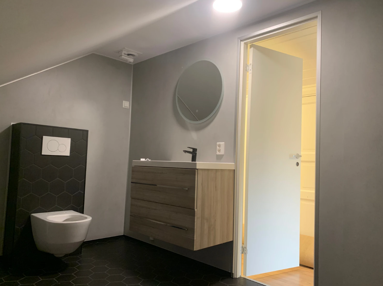 Badet er flislagt på gulv og det er satt inn baderomsplater på veggene. Badet er utstyrt med gulvvarme, dusjhjørne, innfellbare dusjdører, mekanisk avtrekk, opplegg for vaskemaskin, servant, servantskap og veggmontert wc. Galleribilde