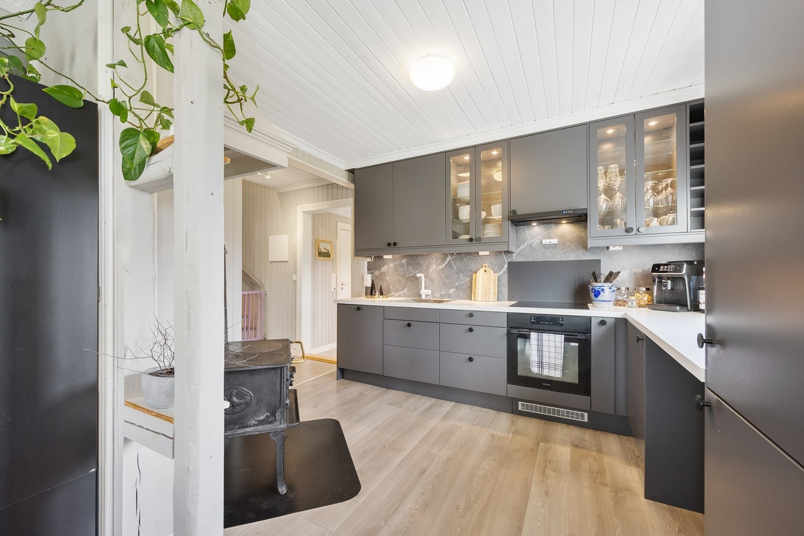 Den takhøye innredningen har grå, glatte fronter, vitrineskap og laminatbenkeplate med oppvaskkum. Galleribilde