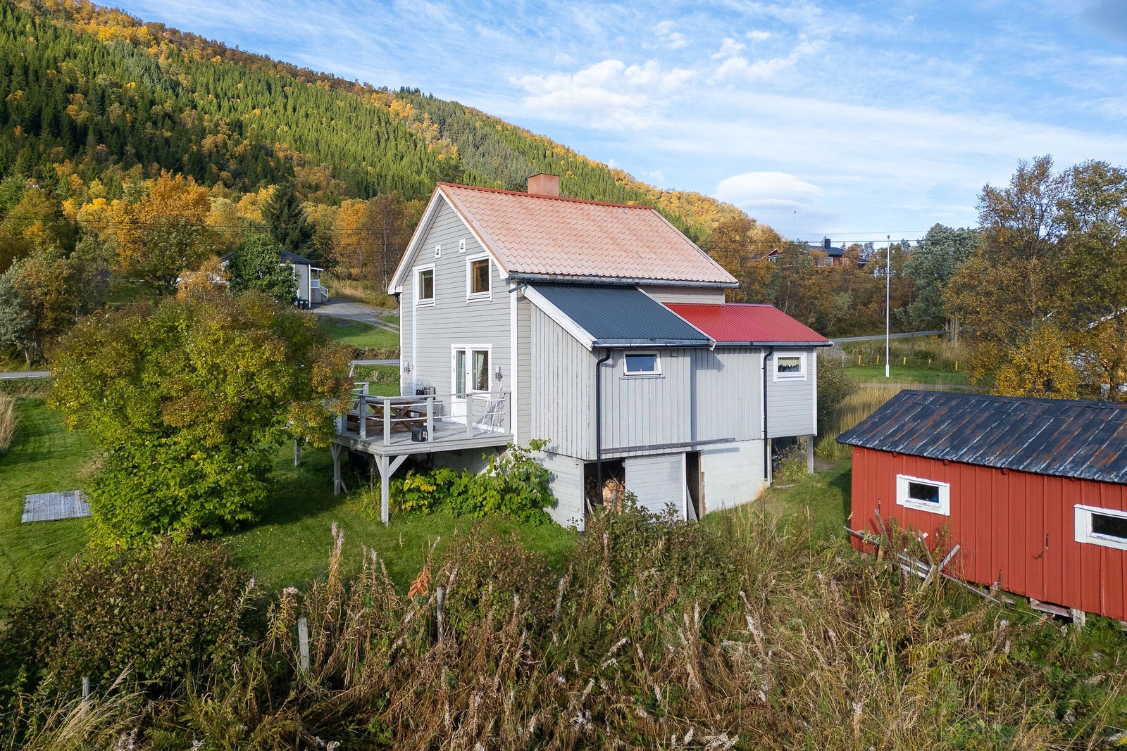 Fasade og uteområde. Boligen står på en lett hellende tomt som er delvis opparbeidet med plen og grusede trafikkarealer. Galleribilde