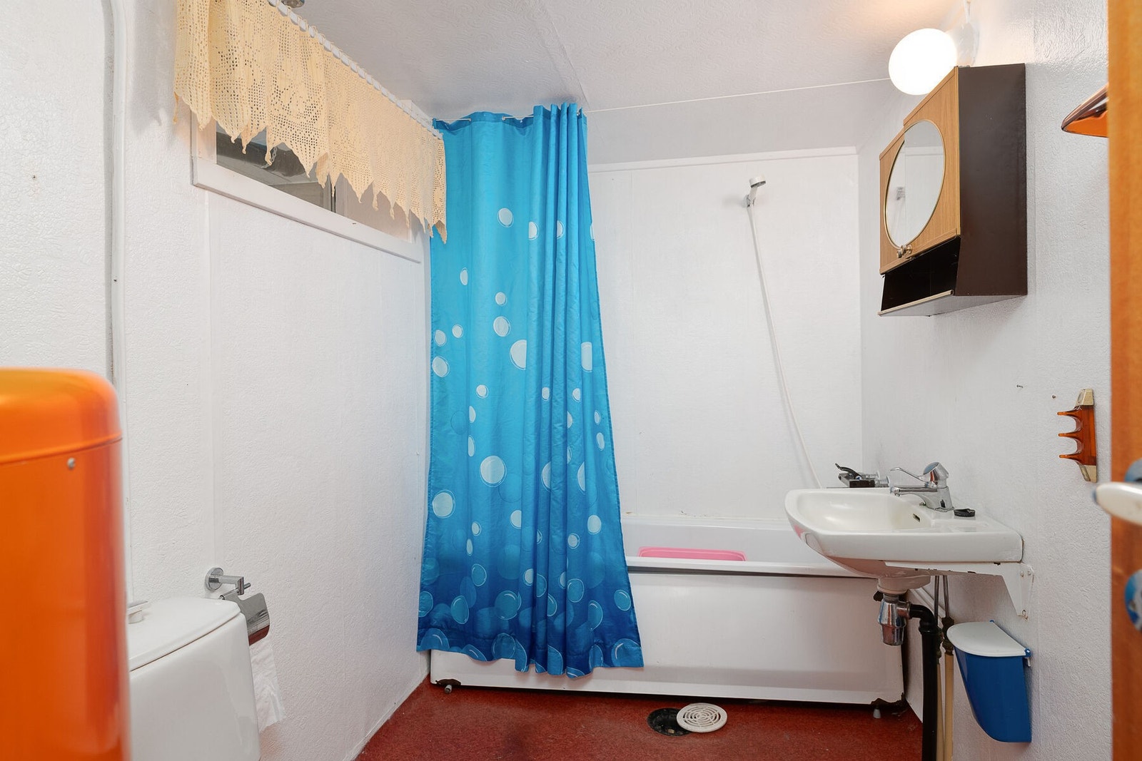 Eldre bad i kjeller, utstyrt med servant, badekar med dusj og forheng, og gulvmontert toalett. Galleribilde