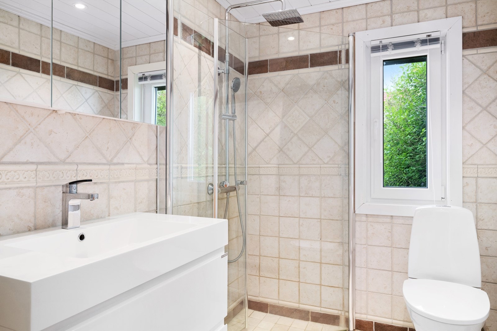 Lyst og innbydende bad med vegghengt servantskap, toalett og dusjhjørne. Galleribilde