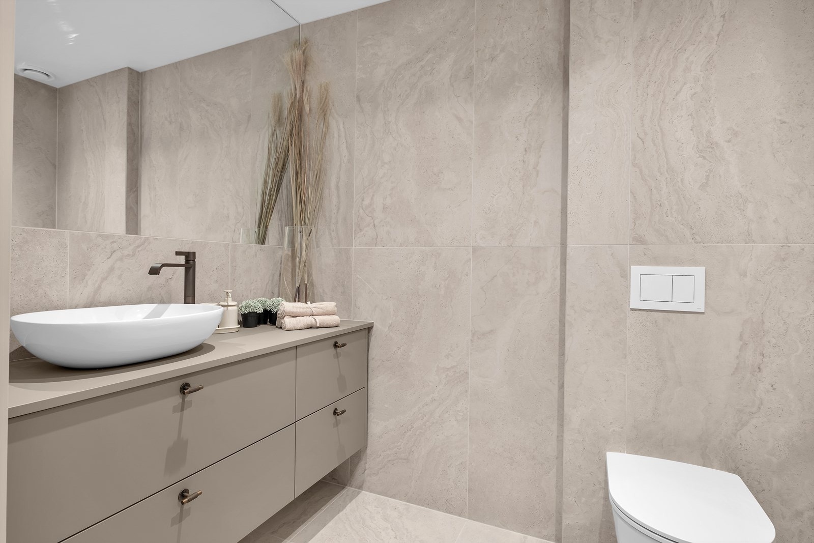 Badene er elegant flislagt med keramiske fliser på både gulv og vegger, og inkluderer moderne baderomsinnredning som speil, servant og vegghengt toalett Galleribilde