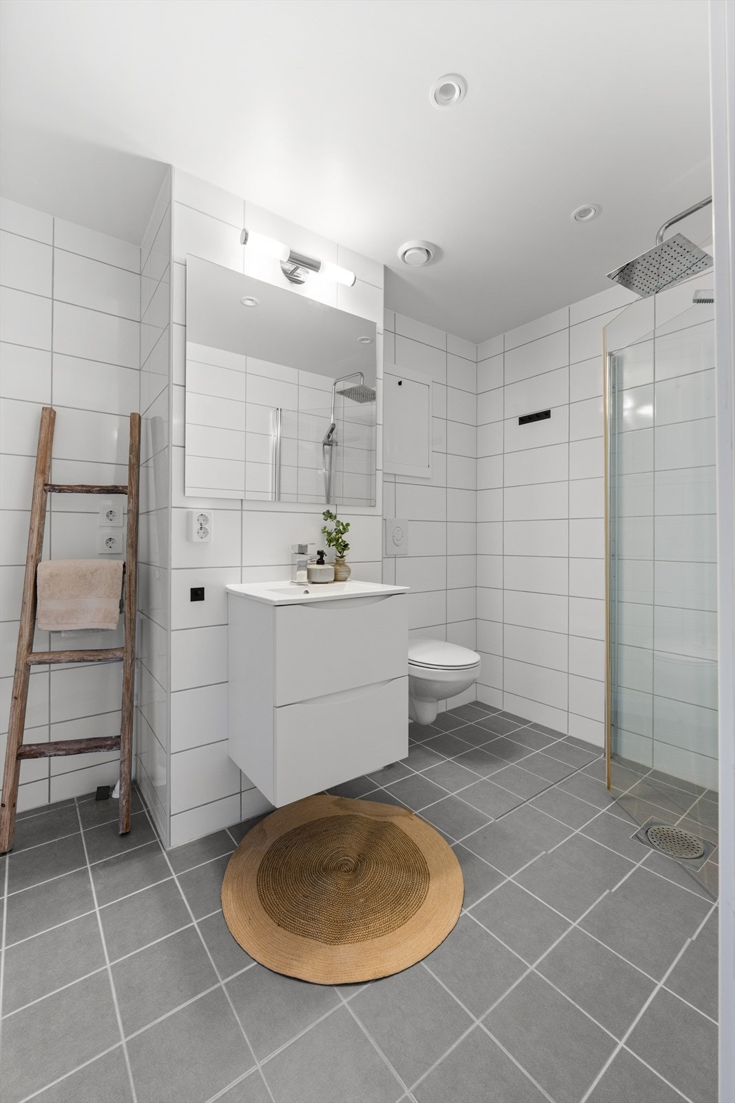 Badet er tidsriktig innredet med heldekkende nedfelt servant med skuffeseksjon, speil, toalett og dusjhjørne med regnfalldusj og innfellbare dusjvegger. Galleribilde