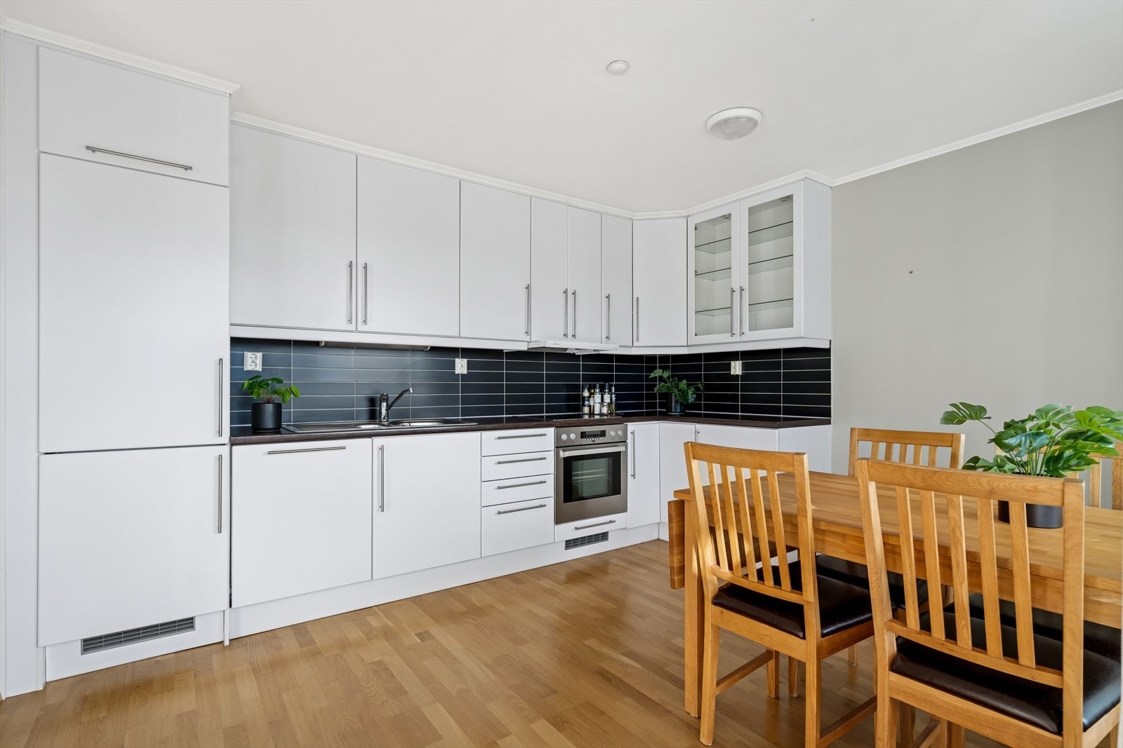 Kjøkkeninnredning med glatte fronter og fliser på vegg over benk. Galleribilde