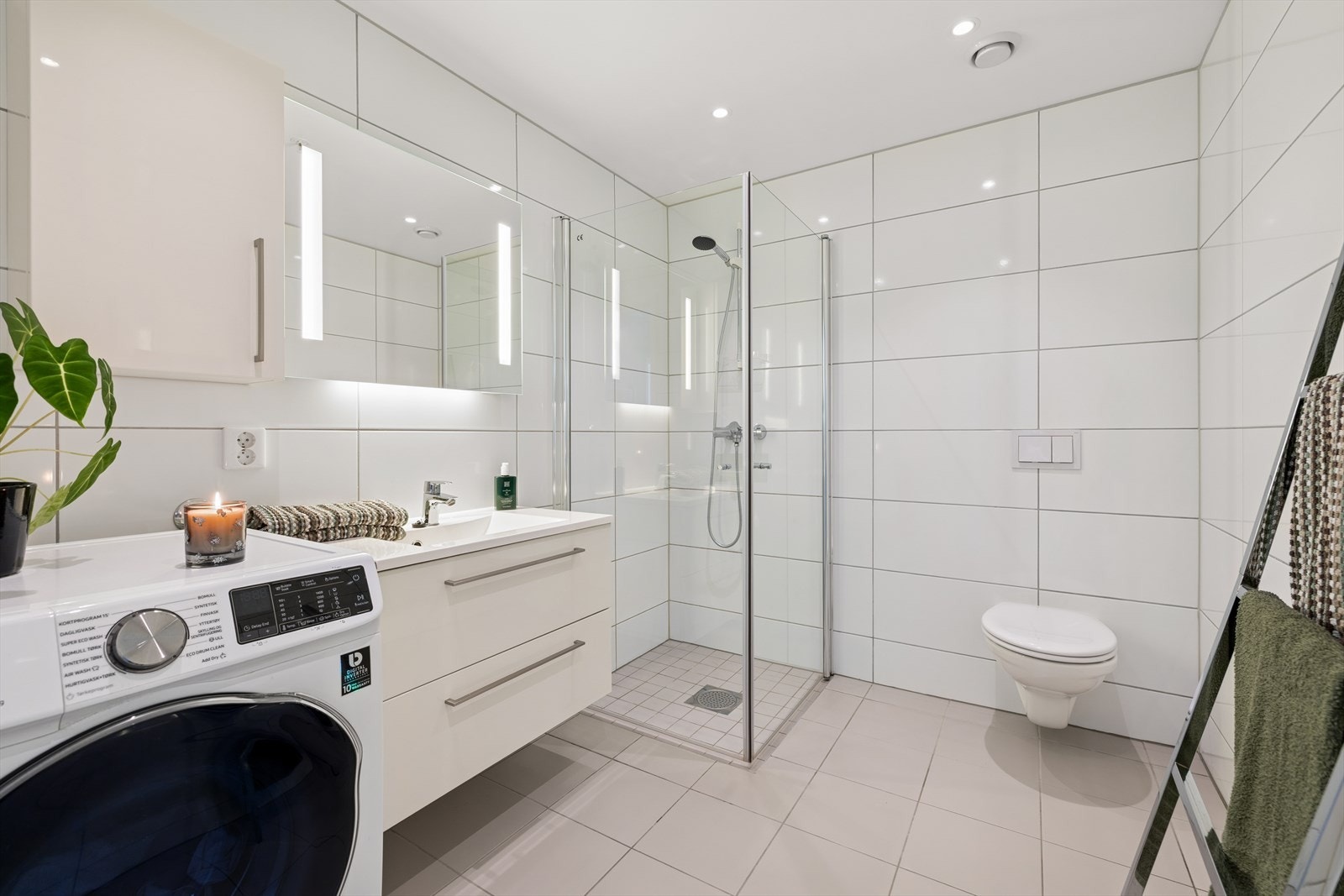 Flislagt baderom med termostatstyrt gulvvarme og downlights i taket. Badet er utstyrt med vegghengt toalett, dusjhjørne med glassdører, baderomsinnredning med servant, samt opplegg for vaskemaskin. Galleribilde