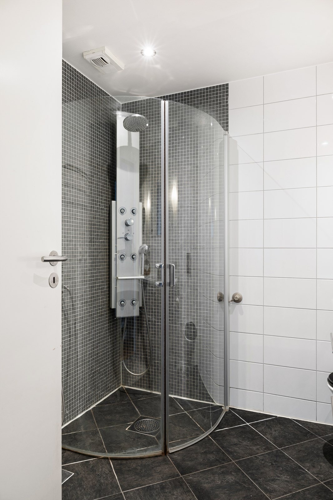 Det er helfliset og har vegghengt toalett, dusjhjørnet med glass dører, servant med underskap og overhengt speil. Videre har badet gulvvarme og opplegg for vaskemaskin. Galleribilde