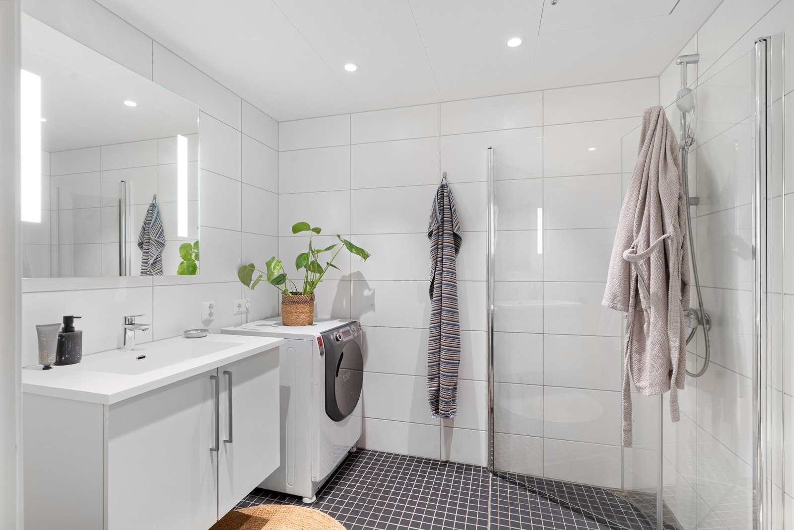 Baderommet er pent innredet med mørke flis på gulv og lyse rektangulære flis på vegg, for et eksklusivt velværepreg. Det hele forsterkes av velplasserte downlights i himling. Galleribilde