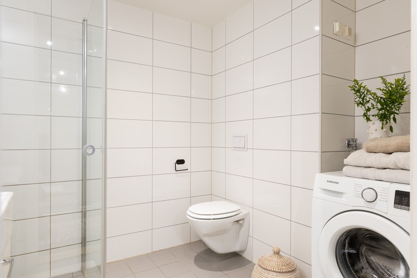 Badet er innredet med vegghengt klosett, servant med innredning, speil m/lys og dusjhjørne med svingbare glassdører. Galleribilde