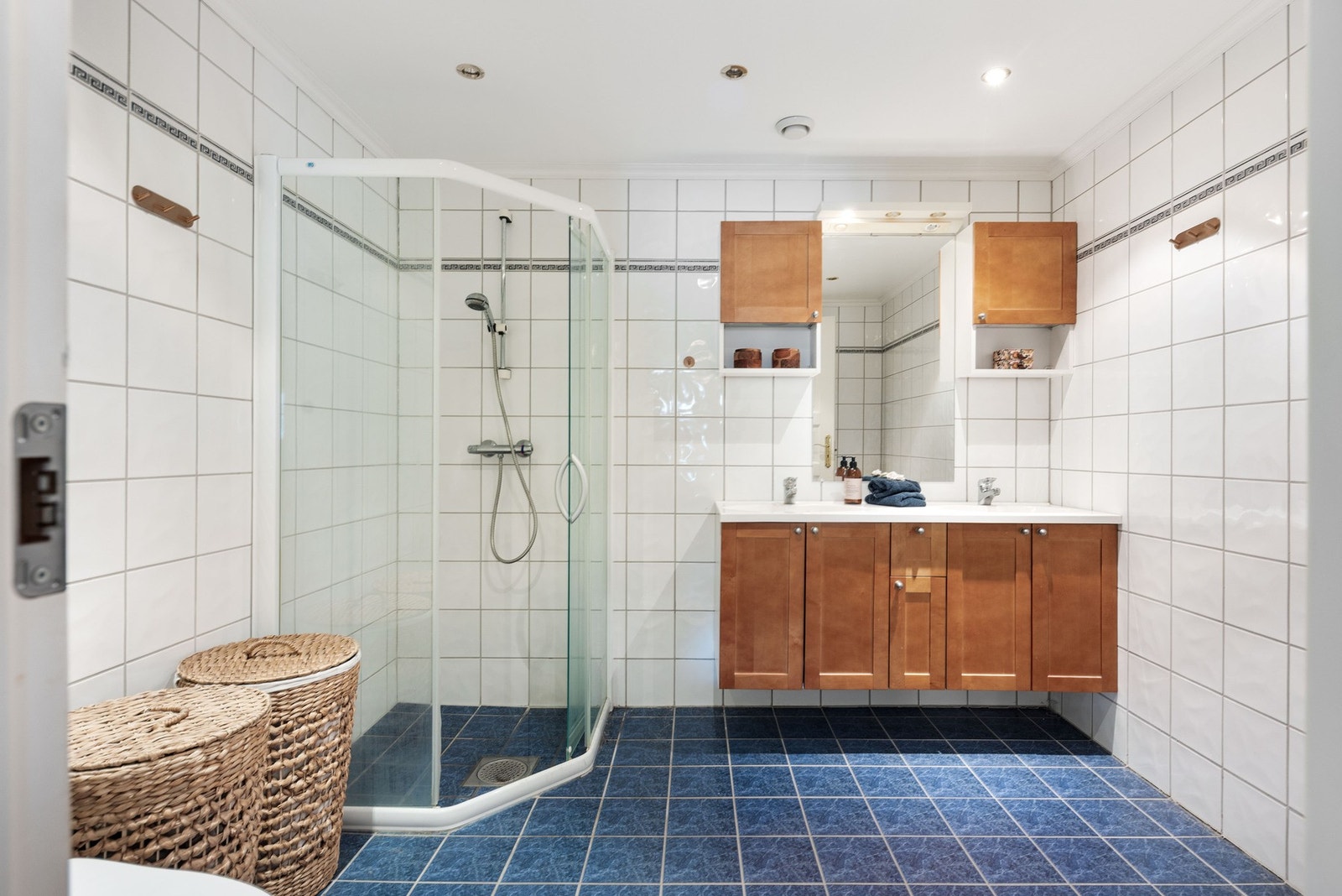 Badet er flislagt med dusj, nedfelt servant med innredning og toalett. Galleribilde