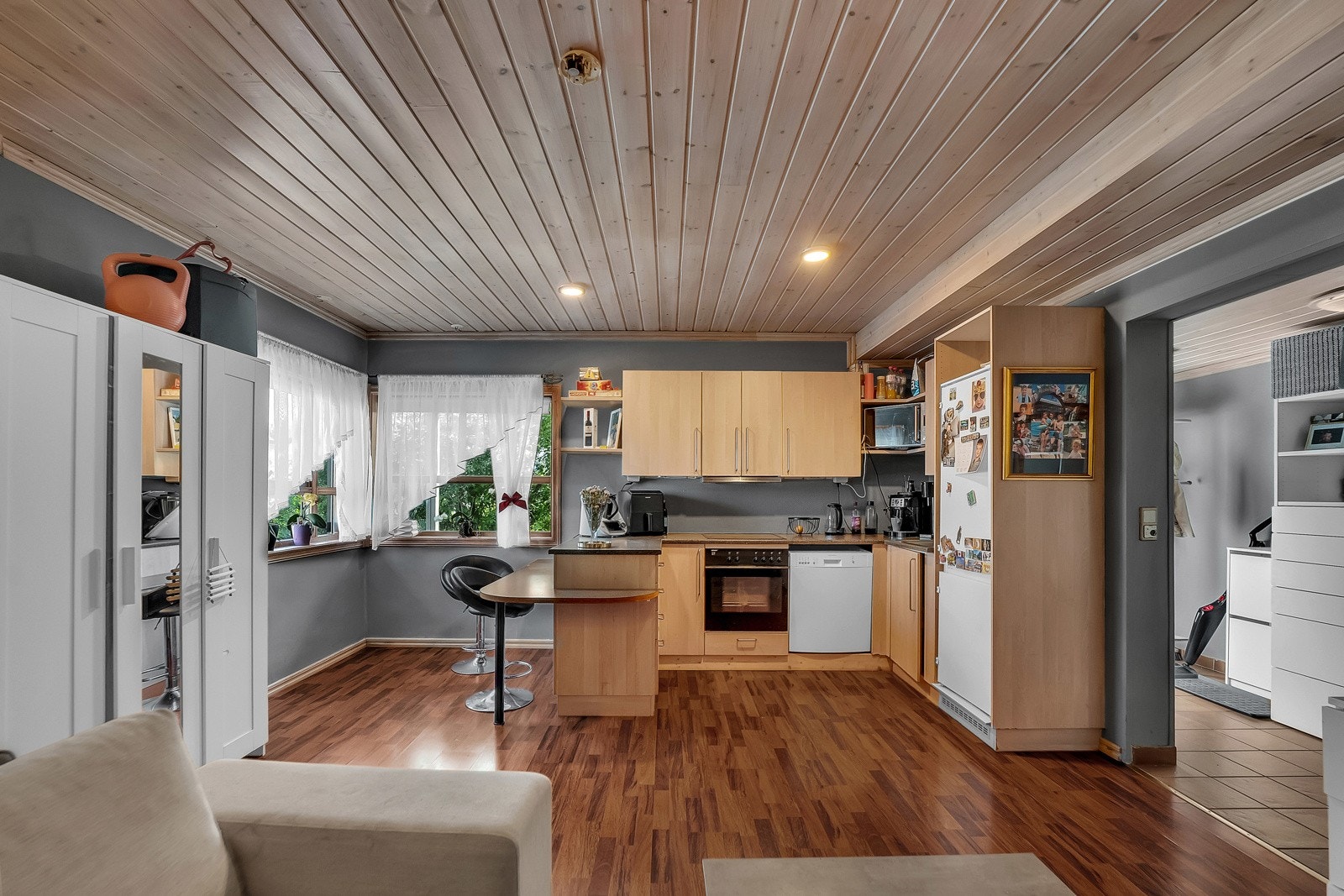 Stuen i utleiedelen har brunt laminatgulv, gråmalte veggflater, lys panelhimling med downlights og gode vindusflater mot hjørnet Galleribilde