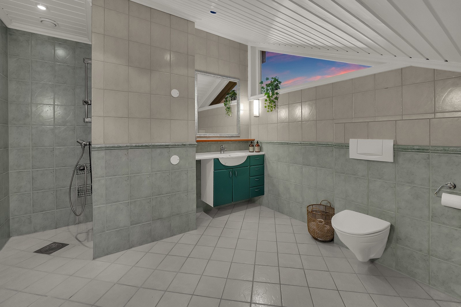 Det grønne badet har servant på et grønnmalt servantskap, speil med hylle og belysning, samt et veggmontert toalett og en dusjnisje. Galleribilde