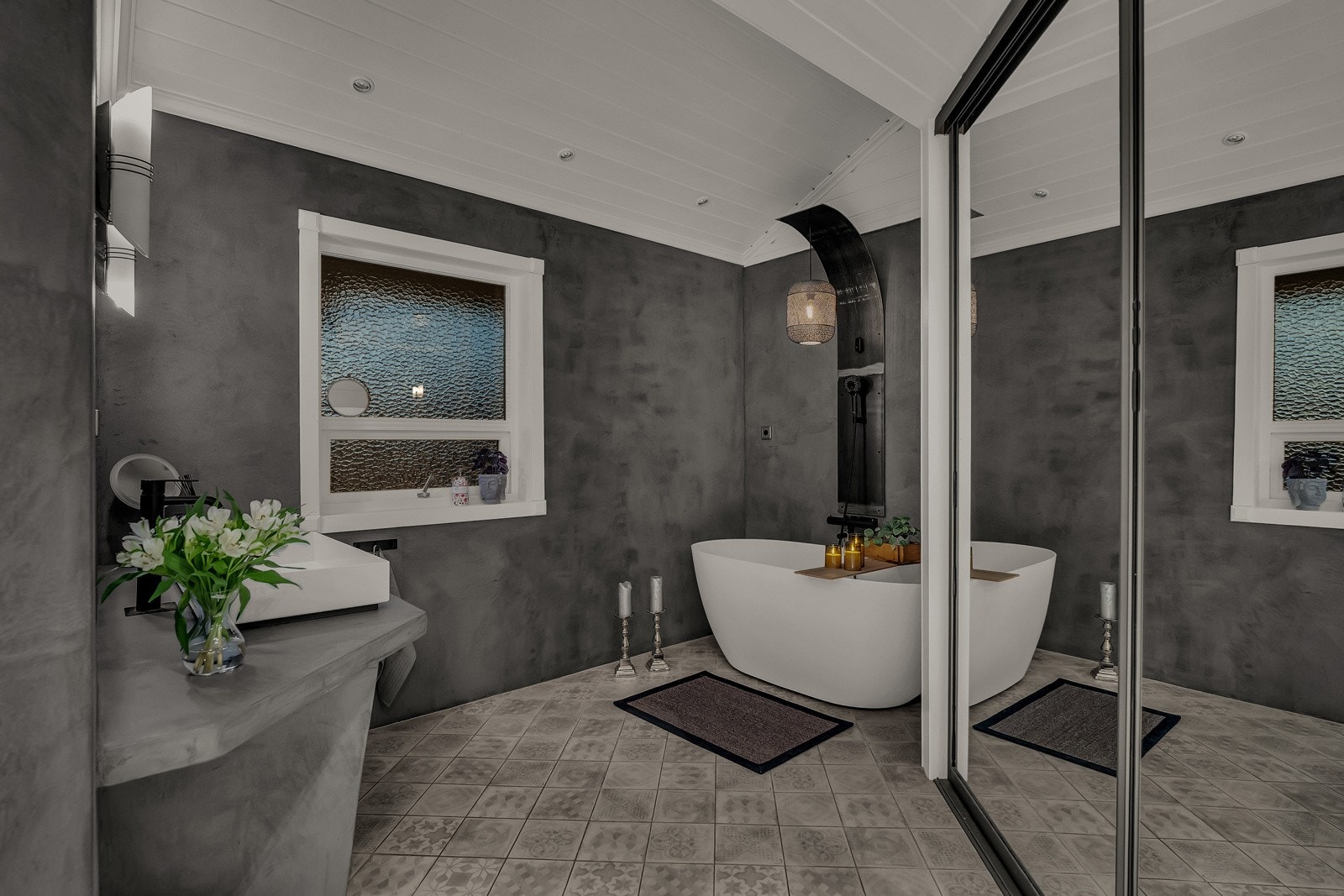 Innredningen består av en toppmontert servant på servantbenk med sementpusset overflate, speil med belysning, et frittstående badekar, samt en dusjnisje med glassdør, regnfallsdusj og hånddusj Galleribilde