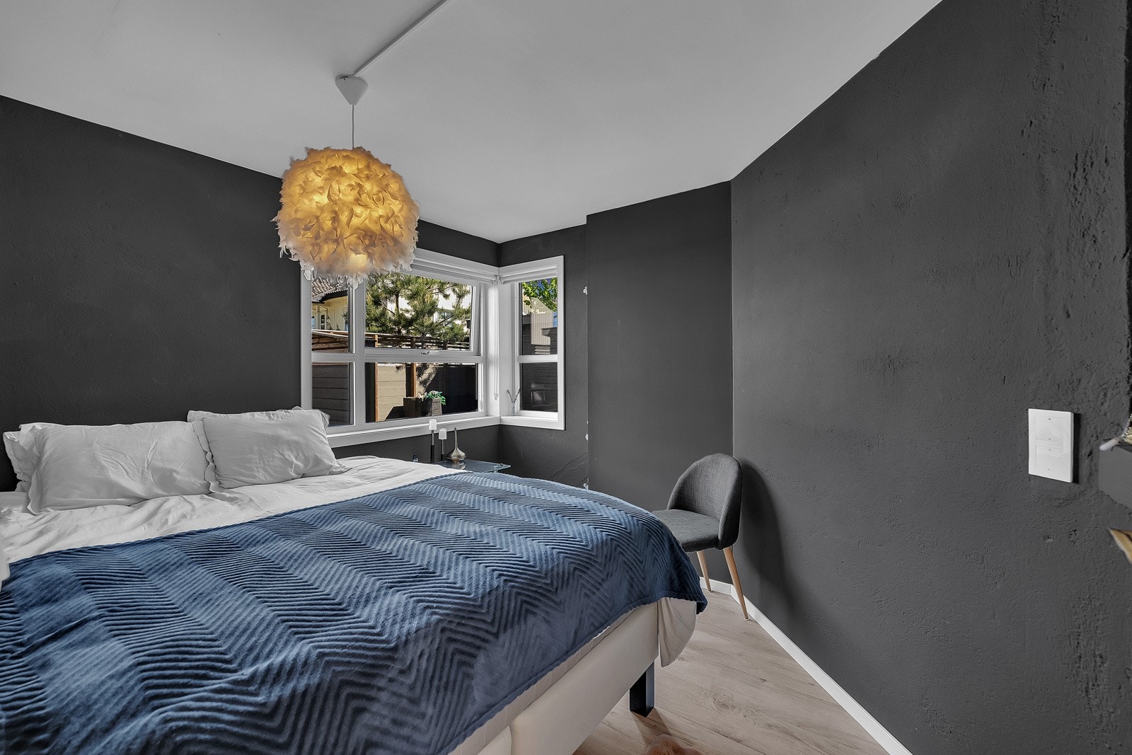 Soverommet i hybelen har mørke veggflater, hjørnevinduer, listefri himling og lyst laminatgulv i enstavs design Galleribilde