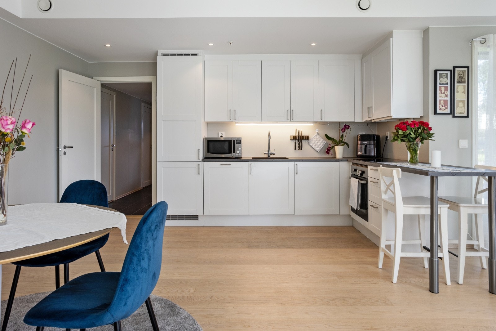 Fra gangen kommer du inn i en romslig, åpen stue- og kjøkkenløsning. Kjøkkenet er moderne utformet med profilerte skapfronter og en solid benkeplate i slitesterkt laminat. Galleribilde