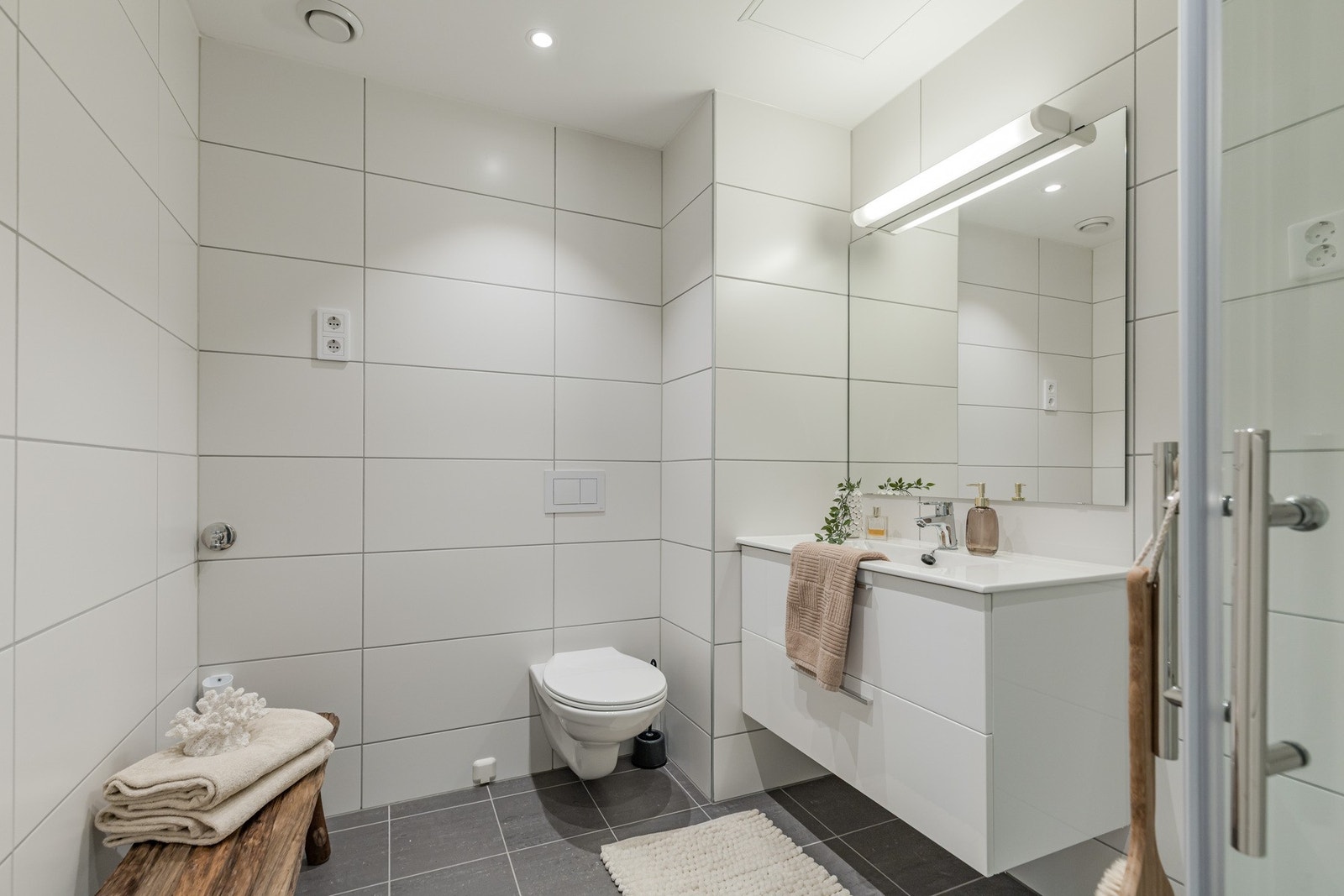 Badet har vegghengt toalett, opplegg for vaskemaskin, servantmøbel med skuffer og speil med lys over. Galleribilde