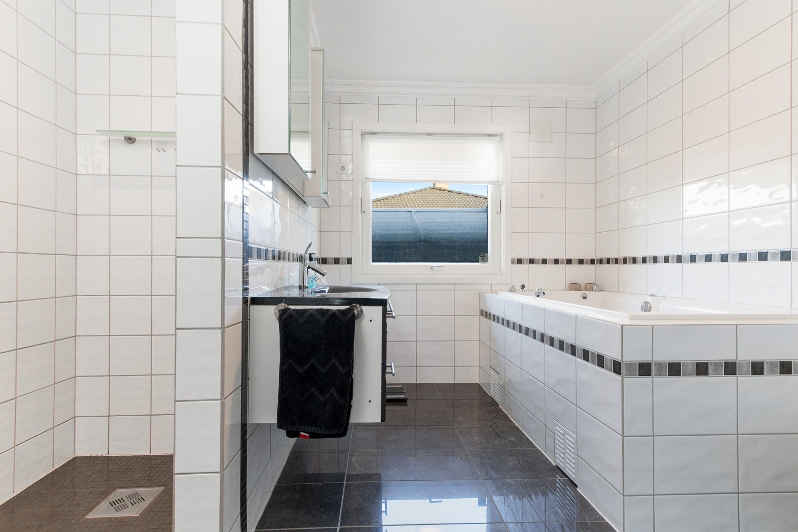 Rommet har mørke fliser på gulvet, lyse fliser på veggene, dusjnisje og et deilig, innfliset boblebadekar. Galleribilde