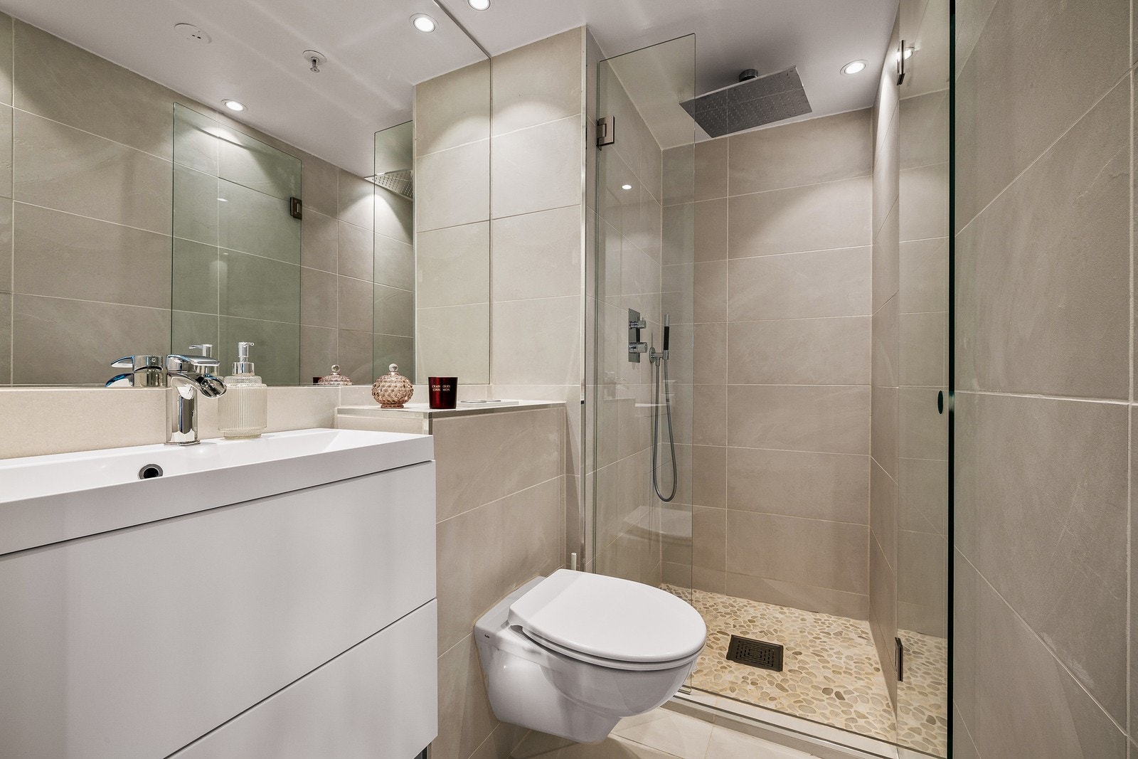 Rainfall- og hånddusj, vegghengt toalett og vakre sandfargede fliser skaper et stilrent og innbydende baderom med spa-følelse Galleribilde