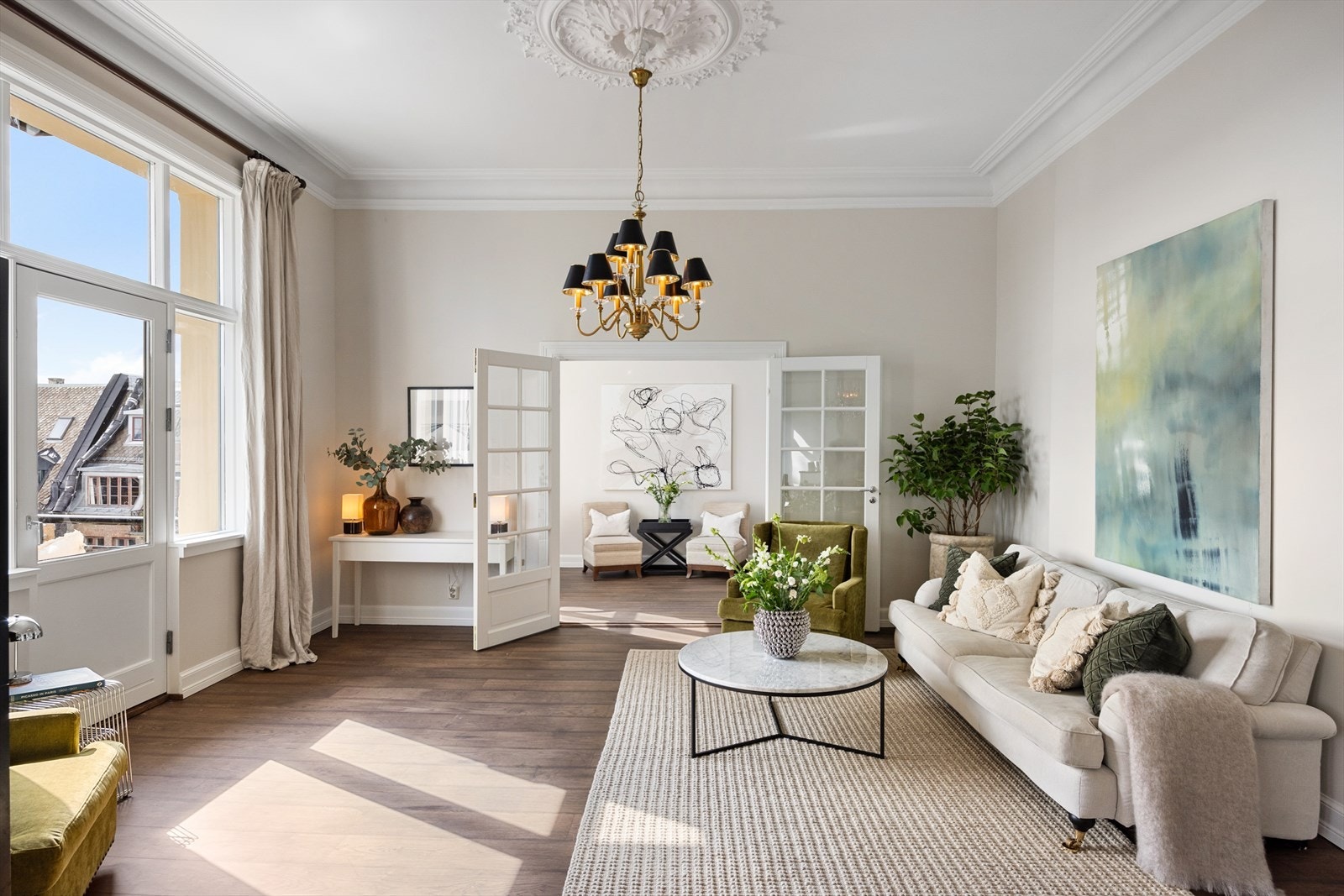 Lys og innbydende stue med god plass til en romslig sofagruppe og øvrig møblement. Det er pipeløp i rommets hjørne ved grønn plante. Galleribilde