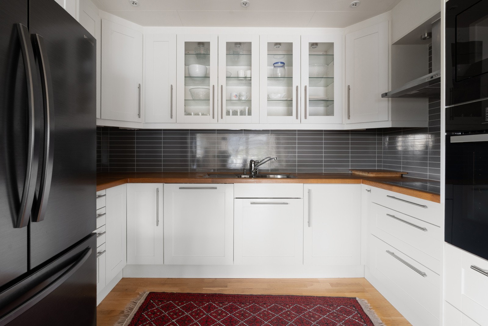 Større kjøkken med heltre benkeplate, flotte lyse fronter, hvitevarer i arbeidshøyde og kjøleskap med isbitmaskin og dobbeldører. Galleribilde