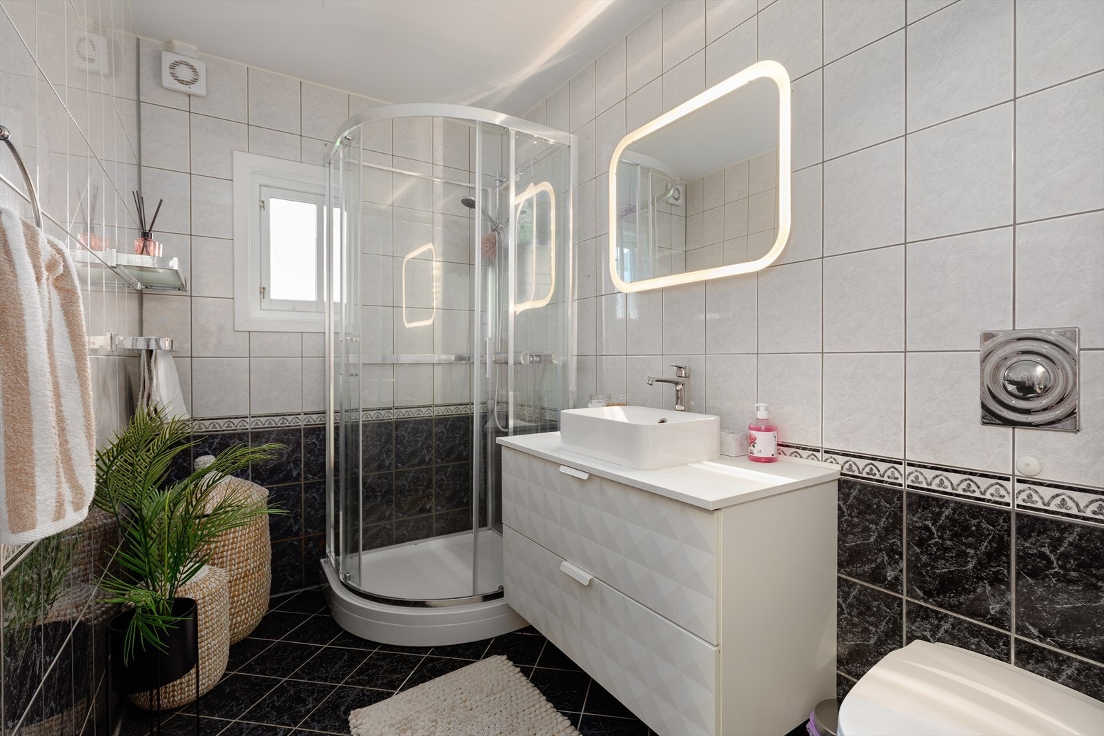 Bad med fliser på gulv og vegger, samt 60x120 himlingsplater. Badet er utstyrt med dusjkabinett, toalett og servant med innredning. Galleribilde