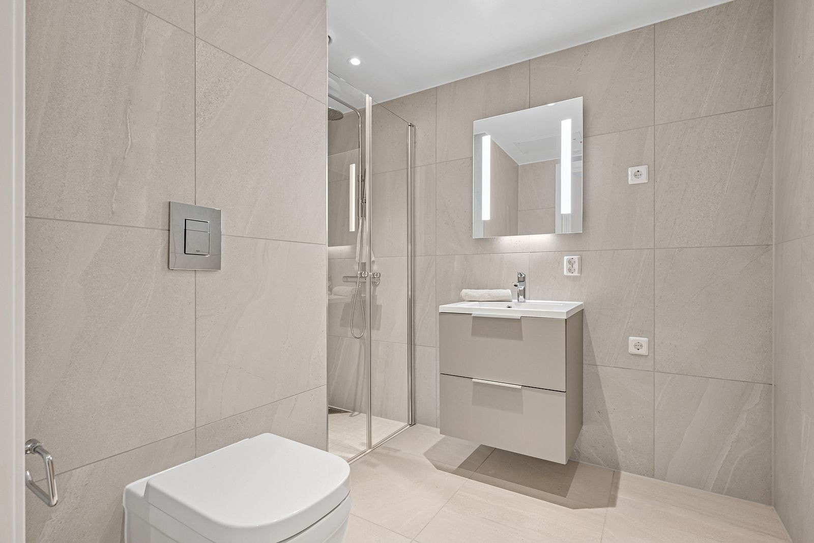 Bad nummer to er elegant og romslig, smakfullt innredet med et vegghengt WC, moderne baderomsmøbler og en stilfull dusjnisje. De lyse beige flisene og de rene linjene gir rommet et sofistikert og minimalistisk preg. Galleribilde