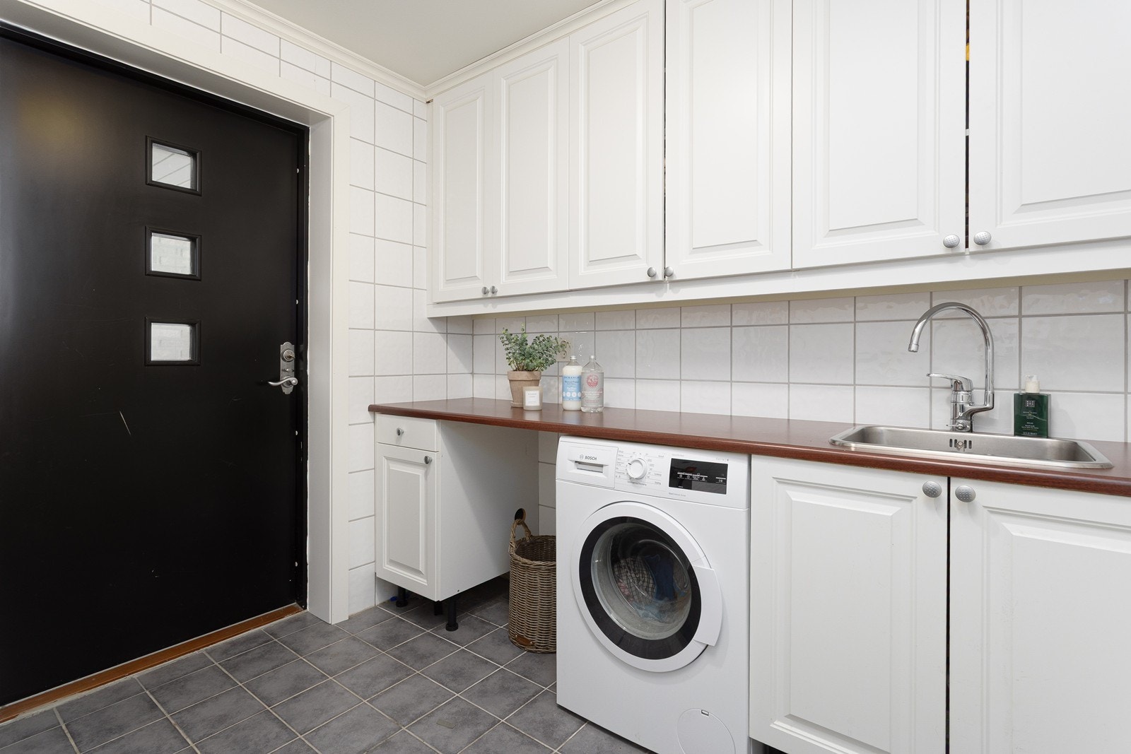 Vaskerommet er smart og praktisk innredet med fliser på gulv og vegger, rikelig oppbevaringsplass og benkeplate til klesbretting. Galleribilde