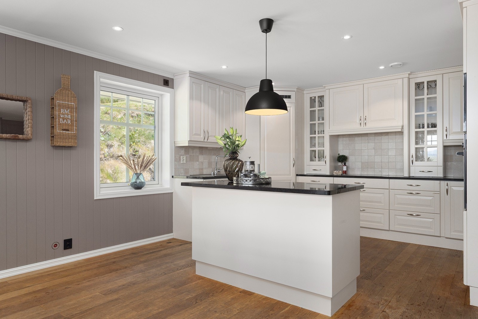 Platetoppen er plassert i en stilig grue med overskap med ventilator, omgitt av takhøye skap med vitrinedører - en gjennomtenkt løsning som kombinerer funksjonalitet med flott design. Galleribilde