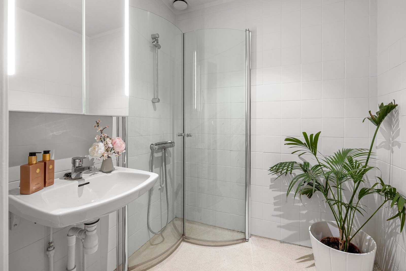 Badet er innredet med dusjhjørne og servant, samt speil med oppbevaring og integrert belysning. Galleribilde