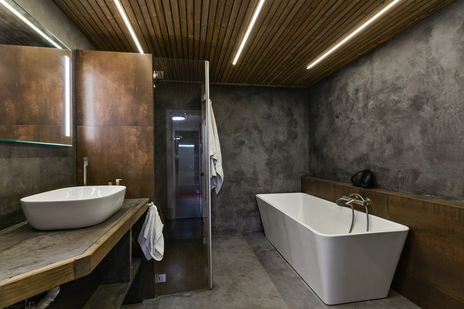 Dusjhjørne med flislagte dusjvegger og sittebenk, innfellbare glassdører samt frittstående badekar Galleribilde