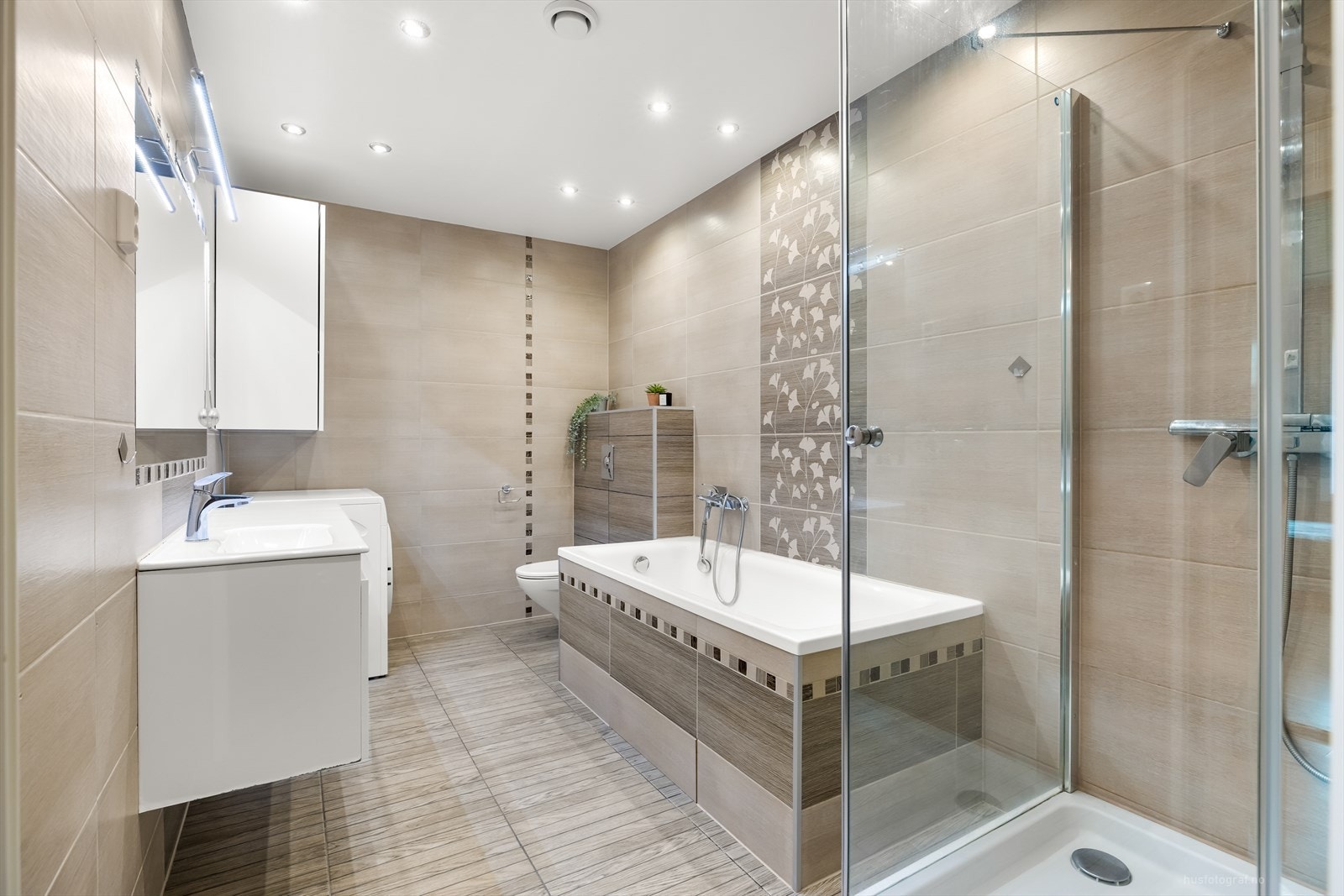 Romslig bad med dusjkabinett, badekar, vegghengt toalett og opplegg for vaskemaskin. Galleribilde