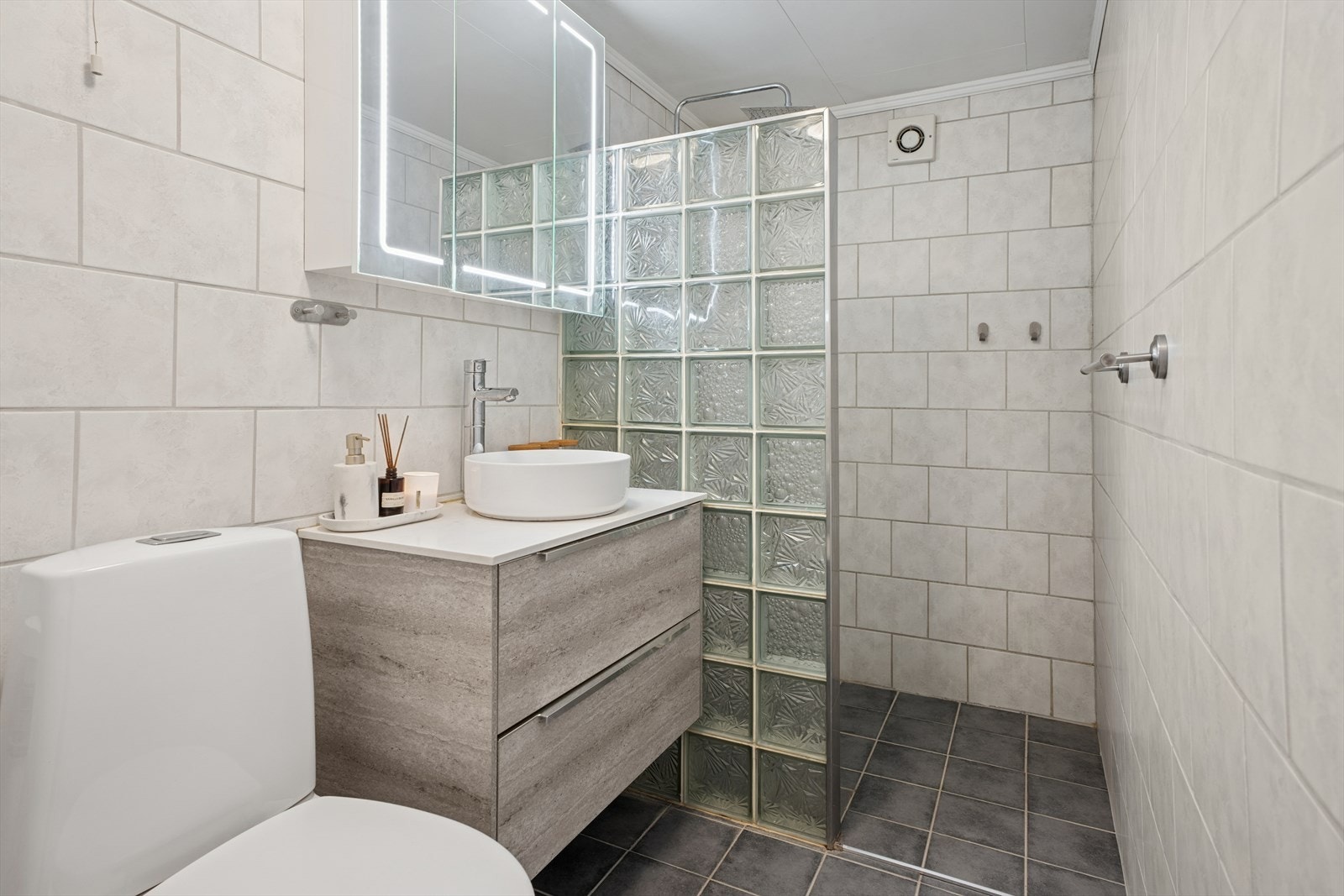 Badet har fliser på gulv og vegger. Det er termostatstyrt varmekabel i gulv. Dusjvegg i glassbyggerstein. Galleribilde