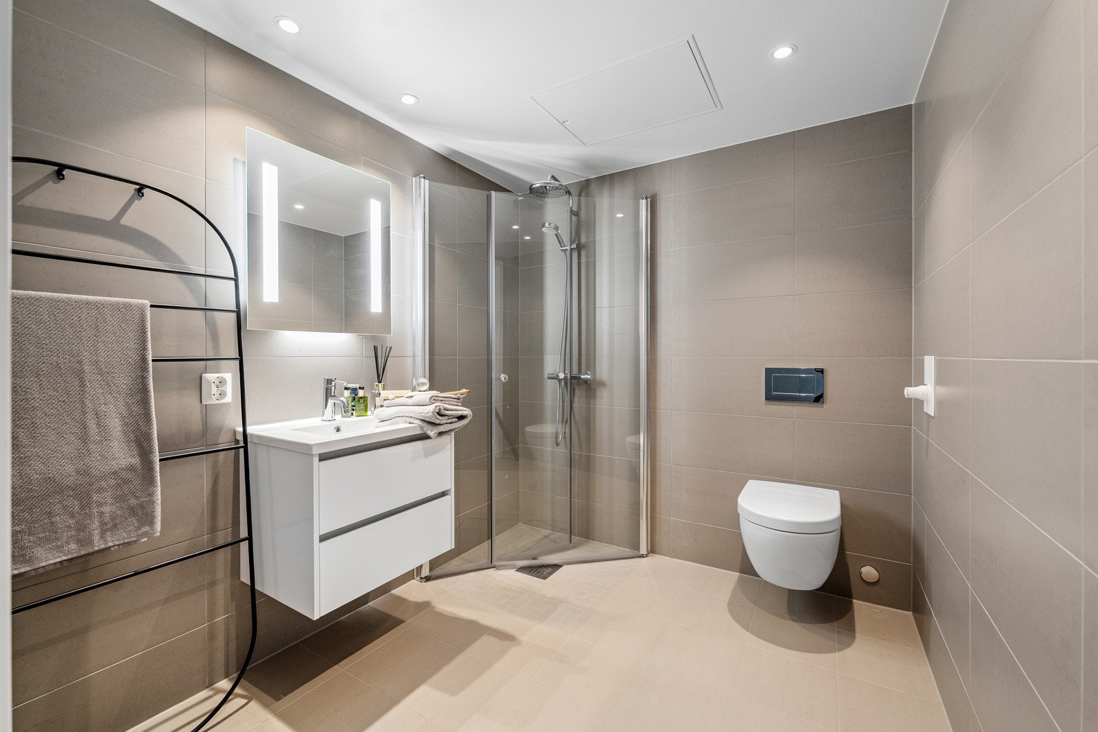 Delikat flislagt bad med vannbåren gulvvarme. Baderomsinnredningen består av servantmøblement med glatte fronter og speil med integrert belysning. Opplegg for vaskemaskin. Galleribilde