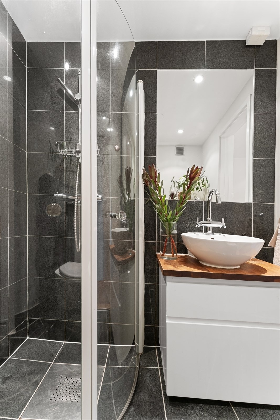 Badet har hjørnedusj med innsvingbare dusjdører i glass, servantinnregning med skuffer, toalett og speil. Galleribilde