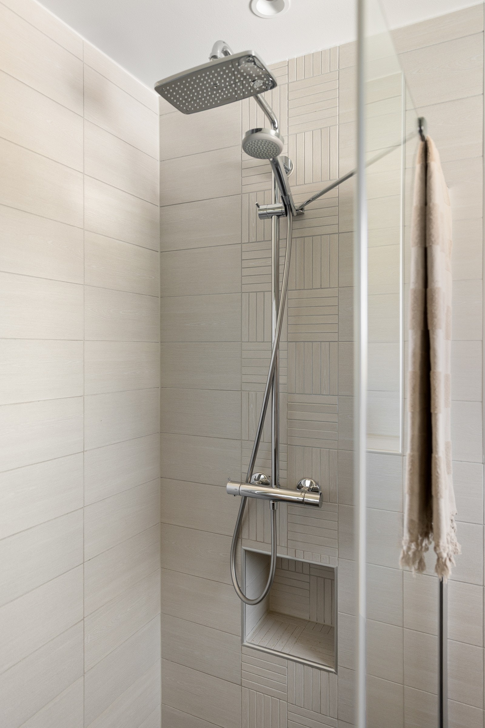 Det har flislagte vegger og gulv, malt tak med downlights, dobbeltservant, dusjhjørne og veggmontert toalett Galleribilde