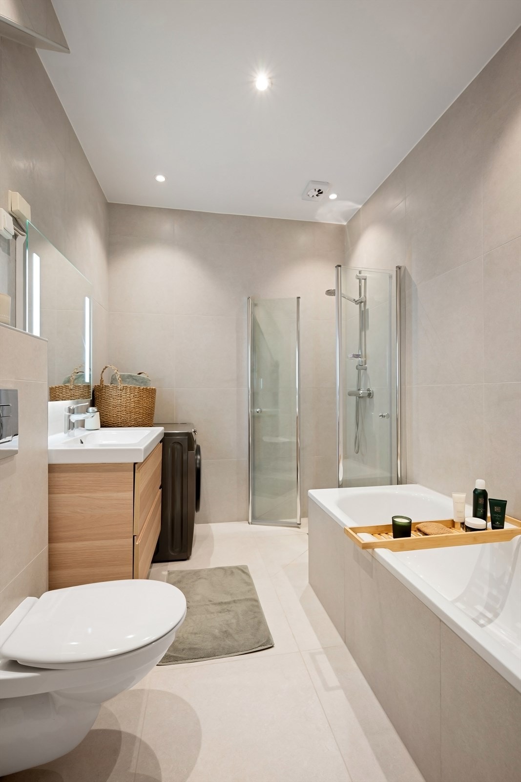 Lyst og pent bad med nedsenket dusjhørne med dører i herdet glass og innmurt badekar. Servant med underskuffer og speil med LED lys over servant. Vegghengt toalett. Mekanisk avtrekk. Galleribilde