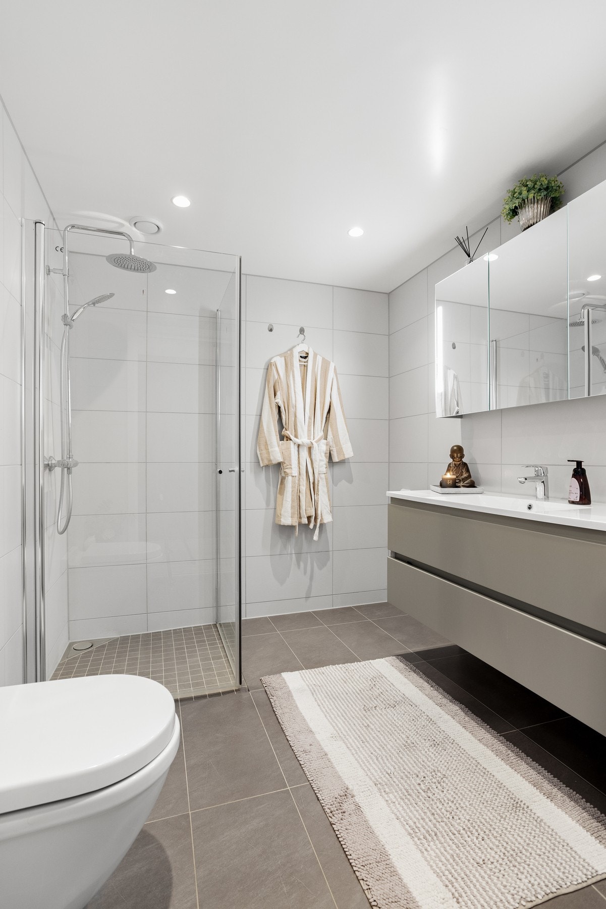 Bad 2 med flislagte vegger og gulv, dusjnisje, veggmontert toalett og innredning med skuff- og skap plass Galleribilde