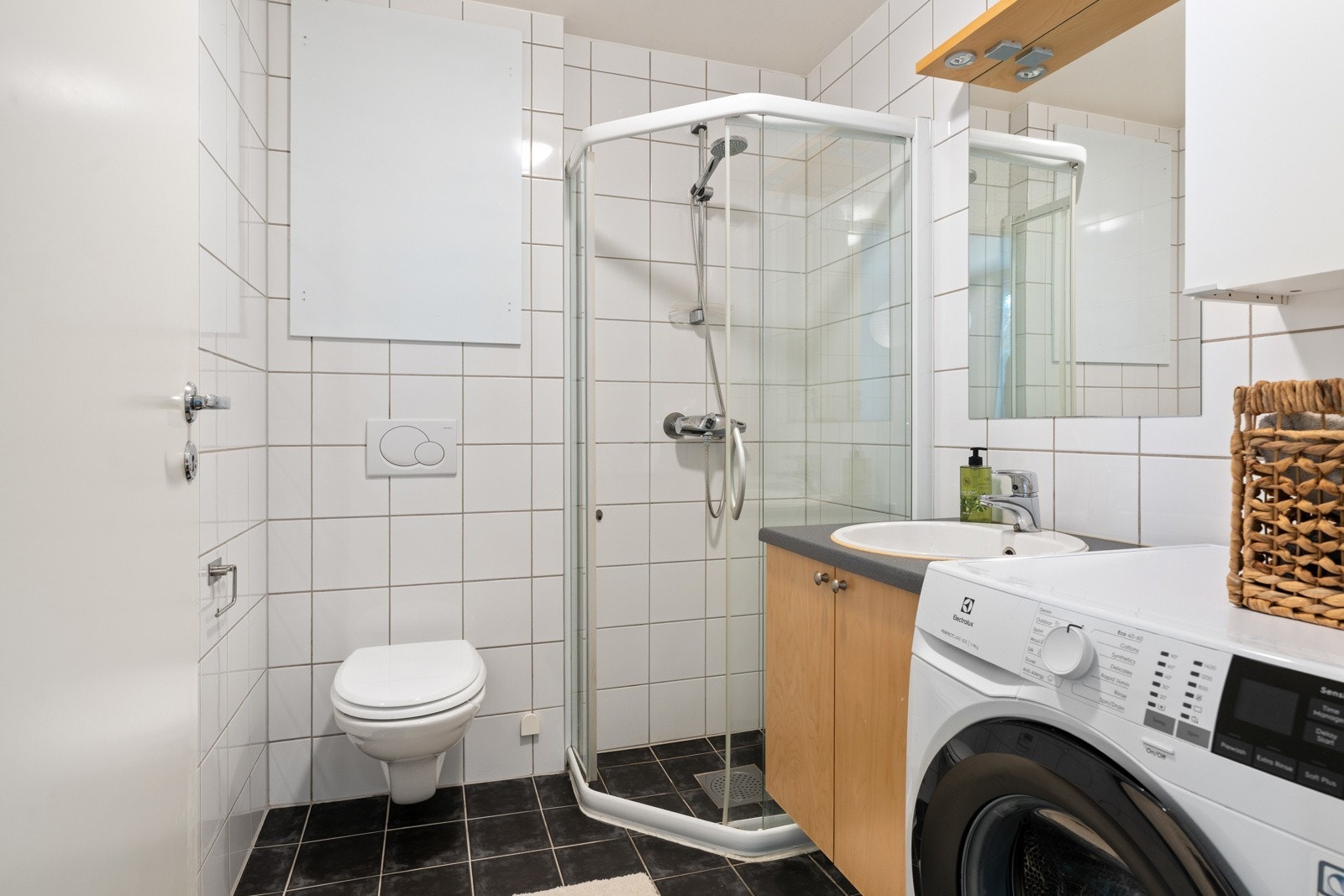 Badet er funksjonelt innredet med dusj med innfellbare dusjvegger, vegghengt toalett, servant med innredning og opplegg for vaskemaskin. Galleribilde