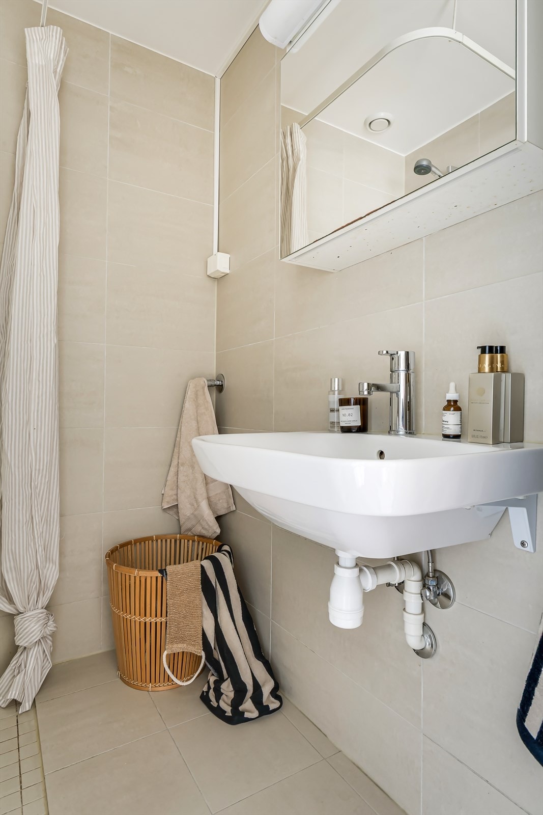 Et lyst bad med flislagte overflater i beige med opplegg for vaskemaskin. Galleribilde